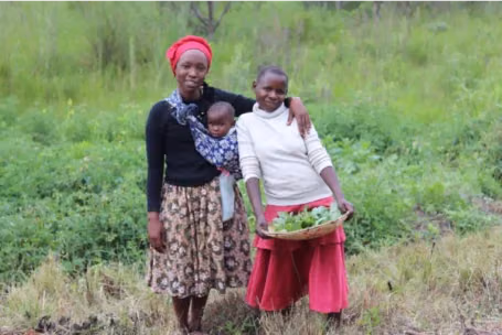 Rythm 20 A woman with a child strapped to her chest stands with a younger woman in a field