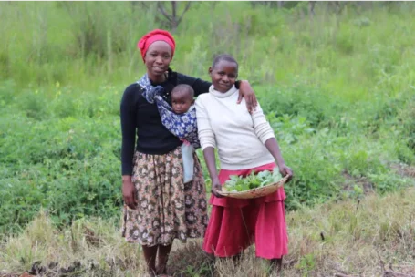 A woman with a child strapped to her chest stands with a younger woman in a field