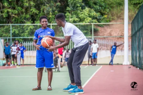 man holding a basketball next to a boy in a volleyball court