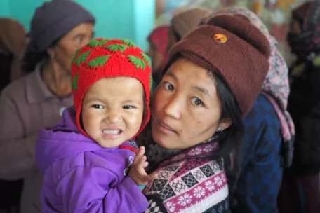 woman holding up her child with a red wool cap